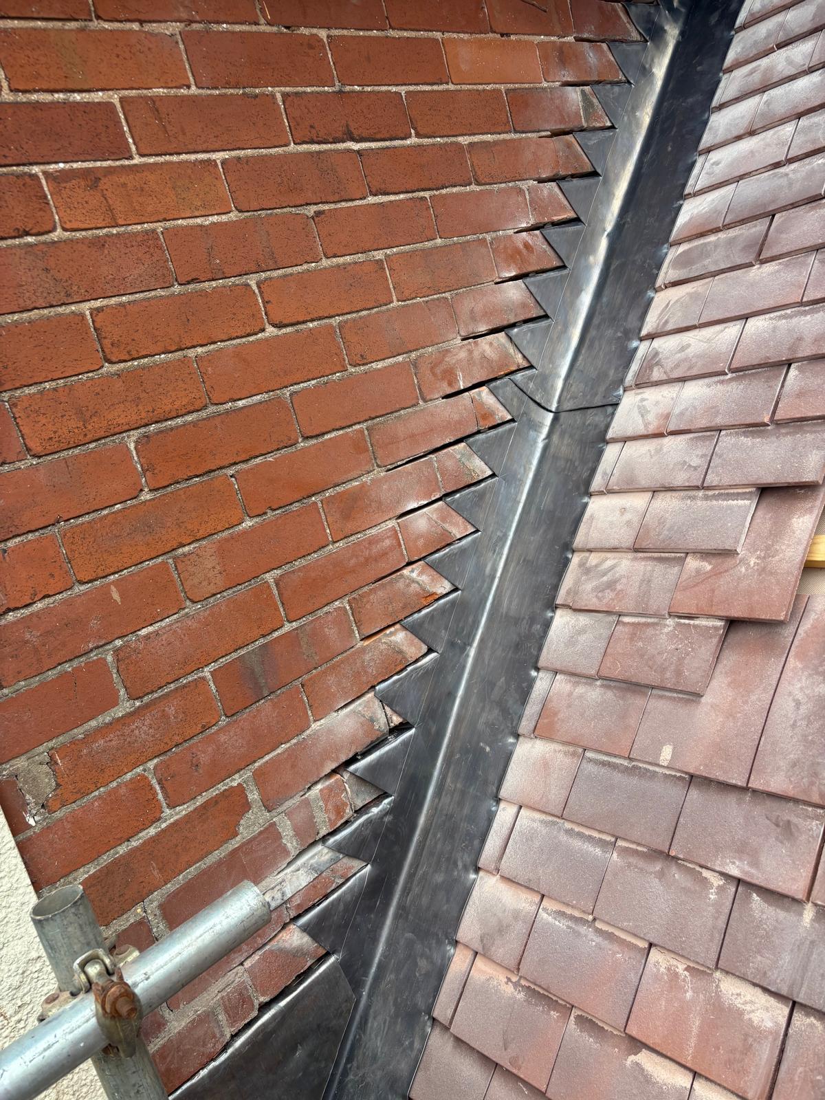 Fresh raked leadwork and stepped flashing where tiled roof meets brick wall